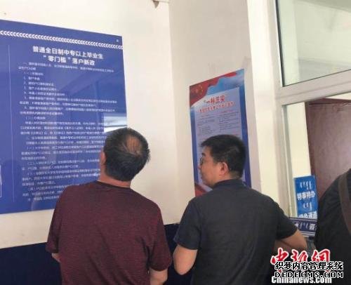图为呼和浩特市新城区东风路派出所中，前来办理户籍登记的市民被墙上的“落户新政”吸引。　陈峰　摄